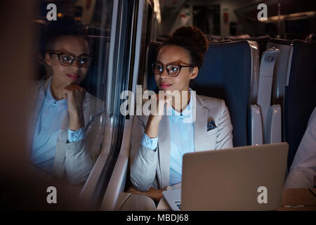 Fiducioso, riflessivo imprenditrice guardando fuori della finestra sul treno passeggeri di notte, lavorando al computer portatile Foto Stock