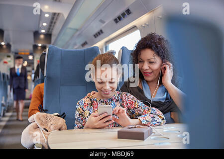 Madre e figlia condividendo le cuffie per ascoltare musica con smart phone sul treno passeggeri Foto Stock