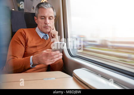 Imprenditore focalizzata usando smart phone al passeggero la finestra del treno Foto Stock