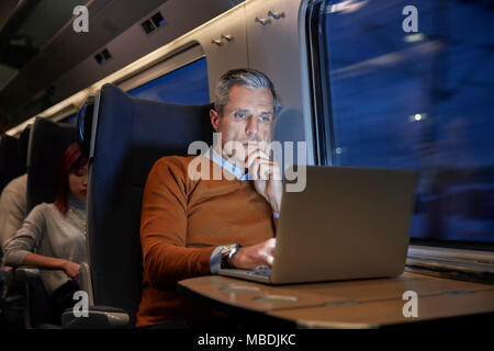 Imprenditore focalizzato lavora al computer portatile sul treno passeggeri di notte Foto Stock