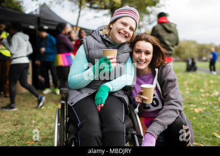 Ritratto di donna sorridente in carrozzina con l'amico, acqua potabile alla gara di carità in posizione di parcheggio Foto Stock