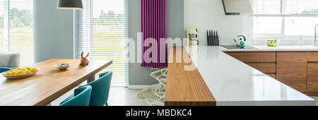 Il ripiano del bancone bianco e viola del riscaldatore nella cucina moderna interno con tavolo da pranzo in legno Foto Stock