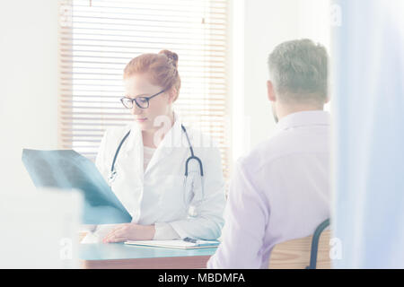 Pulmonologist guardando un'immagine a raggi x del suo maschio i polmoni del paziente nel corso di una consultazione medica Foto Stock