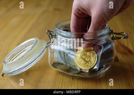 Denaro e jar bitcoin in esso. Mettere mano alle monete in vaso Foto Stock