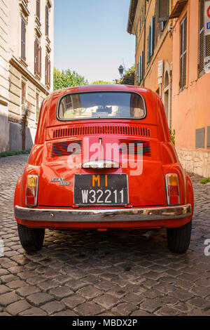 Vista posteriore di un vecchio rosso Fiat 500 parcheggiato in una strada a ciottoli in Italia a Roma al di fuori di un edificio sotto la bandiera italiana. Le targhe mostrano un MI pr Foto Stock