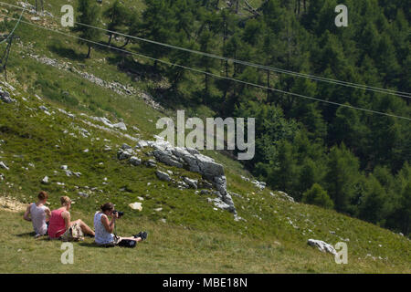 Tre amici seduti ammirando la vista dal Monte Baldo, uno scattare una fotografia, Italia Foto Stock