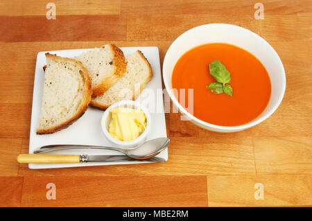Ciotola di zuppa di pomodoro con pane e burro su una piastra su un tavolo di legno, vista dall'alto Foto Stock