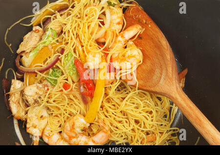 Primo piano di un noodle pollo e gamberi saltare in padella con un cucchiaio di legno in un wok Foto Stock