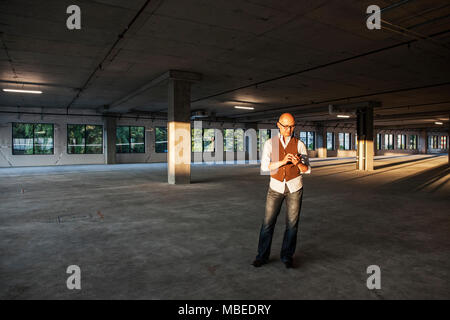 Imprenditore asiatici in piedi in mezzo ad una grande empty Materie di spazio ufficio e illuminato dal tardo pomeriggio sun. Foto Stock