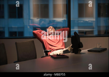 Un imprenditore nera con i piedi su una scrivania mentre lavorando di notte. Foto Stock