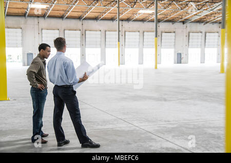 Indietro man proprietario del nuovo magazzino e uomo caucasico architetto andando oltre il blu dei piani di stampa di nuovo layout interni. Foto Stock