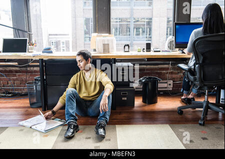 Ispanico uomo seduto su floot net per la sua stazione di lavoro in un ufficio di creative. Foto Stock
