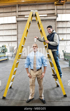 Uomo nero factory proprietario e il giovane uomo caucasico operaio di fabbrica goofing off insieme sul pavimento di una lamiera di fabbrica. Foto Stock