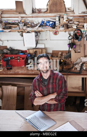 Vista di un sorridente uomo caucasico operaio di fabbrica presso la sua stazione di lavoro in una fabbrica per la lavorazione del legno. Foto Stock