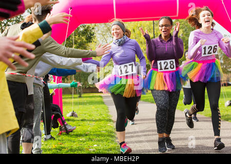 Gli spettatori ad alta fiving femminile in tutus attraversando la carità eseguire il traguardo Foto Stock