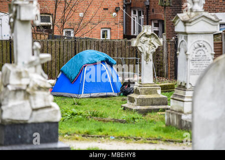 Senzatetto in campeggio in una tenda in un cimitero della chiesa con lapidi funerarie. Piumoni su tela. Chiesa di San Giovanni Battista Foto Stock