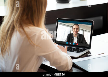 Imprenditrice rendendo la chiamata video al business partner utilizzando laptop. Close-up vista posteriore della giovane donna avente la discussione con il cliente aziendale. Jo remoto Foto Stock