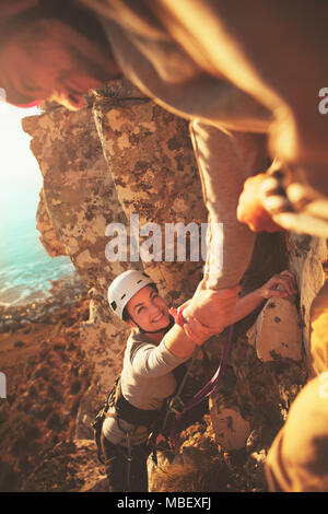 Donna sorridente rocciatore raggiungendo per la mano Foto Stock