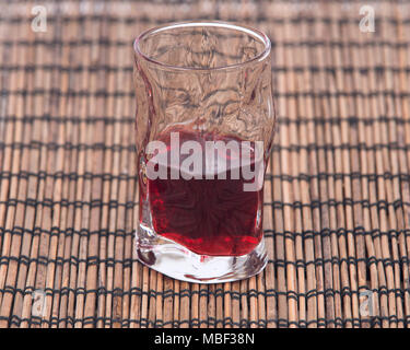 In casa liquore al lampone nel colpo di vetro isolato sul cartellone di bambù Foto Stock