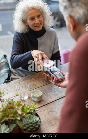 Donna che utilizza smart phone il pagamento senza contatto presso il cafe Foto Stock