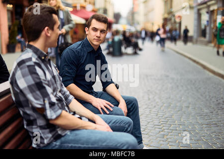 Due uomini di sedersi sulla panchina e talk su strada Foto Stock