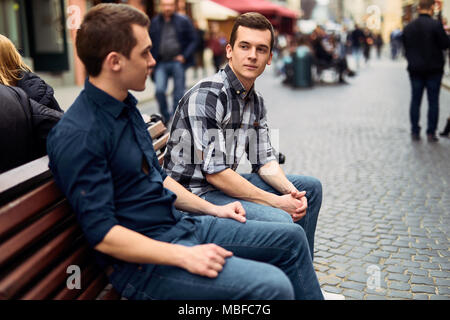 Due uomini di sedersi sulla panchina e talk su strada Foto Stock