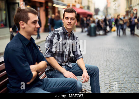 Due uomini di sedersi sulla panchina e talk su strada Foto Stock