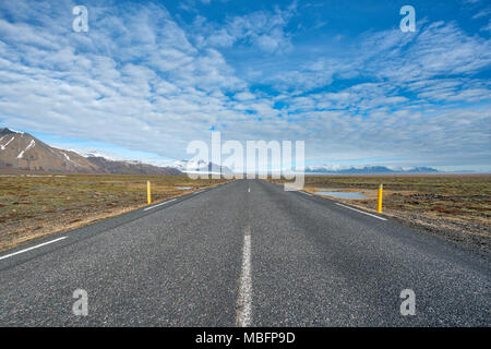 Infinito dritta strada che conduce verso il ghiacciaio e le montagne in giornata soleggiata con metà blu cielo molto nuvoloso in Islanda Foto Stock