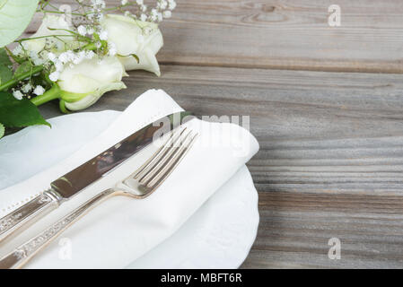 Bella tavola decorati con le piastre bianche, argenteria e white rose fiori su un vecchio tavolo di legno, con copy-spazio Foto Stock