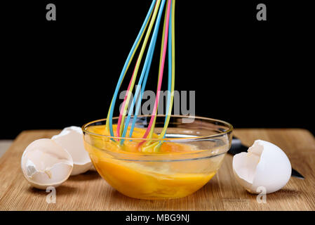 Picchiati i tuorli in una ciotola con la frusta colorati in una ciotola di vetro Foto Stock