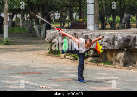 Un uomo cinese sguaina due spade come egli pratica le arti marziali in Yangshuo Park, Yangshuo, Cina. Foto Stock