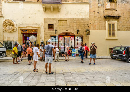 Turisti si riuniscono al di fuori di negozi di souvenir e articoli da regalo nell'antica città di Mdina sull'isola mediterranea di Malta Foto Stock