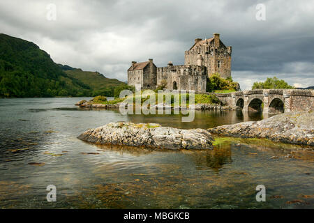 Sole splende attraverso le nuvole sul Castello Eilean Donan con rocce in primo piano loch. Dornie, Scozia Foto Stock