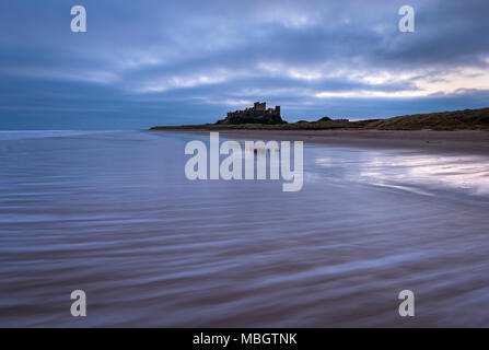 Il castello di Bamburgh illuminato nella pre-alba luce sulla costa di Northumberland. Foto Stock