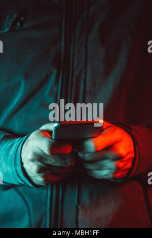 Verticale shot ritagliata della persona di sesso maschile utilizza lo smartphone, di rosso e di blu accesa bassa fotografia chiave Foto Stock