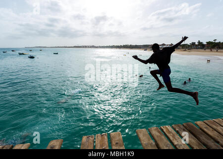 Boy jumping al blu oceano da un molo in legno a Santa Maria, Sal, Capo Verde, Cabo Verde Foto Stock