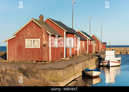 Porto Gammalsby a eastern Oland, Svezia. Rossa piccola pesca in legno cabine in una fila sul molo con piccole imbarcazioni ormeggiate in porto la sera sunlig Foto Stock