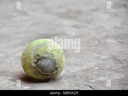 Usurati palla da tennis sul pavimento di cemento con alcuni capelli e piuma su di esso Foto Stock