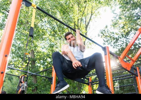 Potente giovane uomo che fa un braccio-pull-up mentre è appesa su una barra in posizione di parcheggio Foto Stock