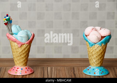 Blu e rosa meringa in rosa e in blu coni con tortine su tavola di legno sfondo bianco Foto Stock