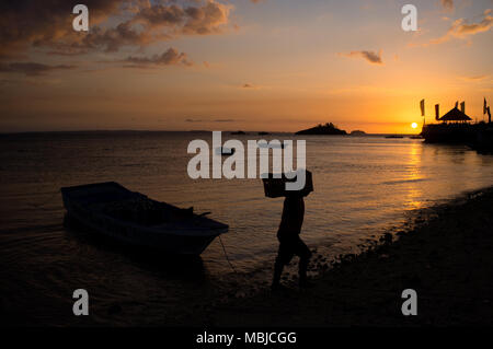 Un uomo porta le forniture di cibo e bevande a terra da una barca al tramonto sulla isola di Malapascua, Daanbantayan, Filippine. Foto Stock