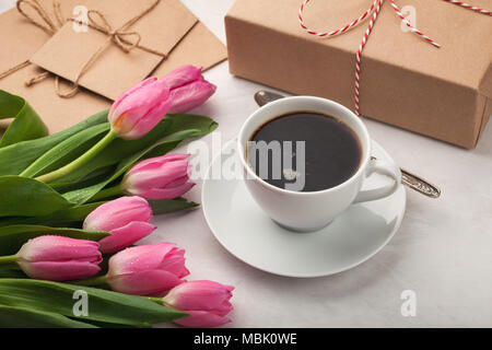 Tulipani rosa, una tazza di caffè e un regalo su una pietra di luce sullo sfondo. Concetto di primavera Foto Stock