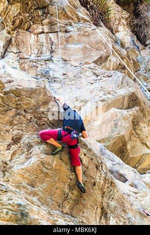 Giovane uomo arrampicata su una parete di roccia Foto Stock