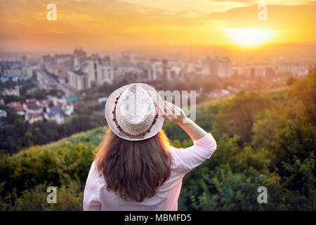 Donna in hat guardando il tramonto. vista città sullo sfondo