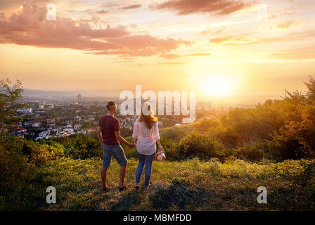 Yong giovane in abiti rosa azienda dalle mani e guardando il Sunset City Foto Stock