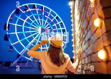 Tourist woman in hat guardando incandescente ruota panoramica Ferris di notte Foto Stock