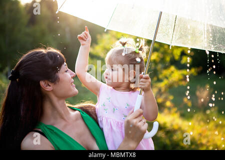 Felice famiglia divertenti con ombrello sotto la doccia d'autunno. La ragazza e sua madre sono godendo di pioggia. Kid e la mamma stanno giocando sulla natura all'esterno. Foto Stock