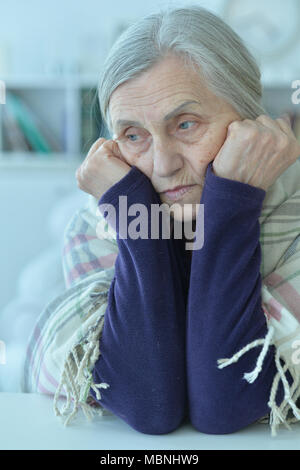 Triste senior donna seduta a tavola Foto Stock