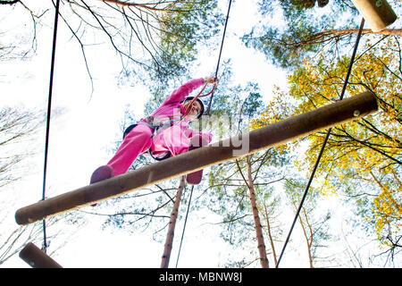 Giovane ragazza nel cablaggio di arrampicata e cercando strutture in un parco avventura. Foto Stock