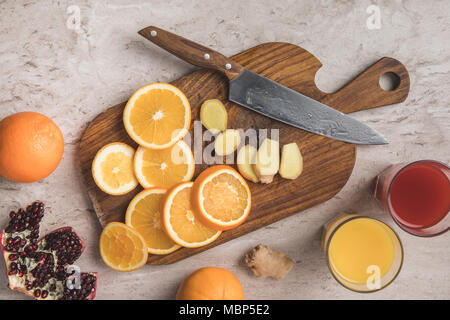 Vista dall'alto di tagliare le arance, zenzero e melograno con succhi fatti in casa sul tavolo Foto Stock